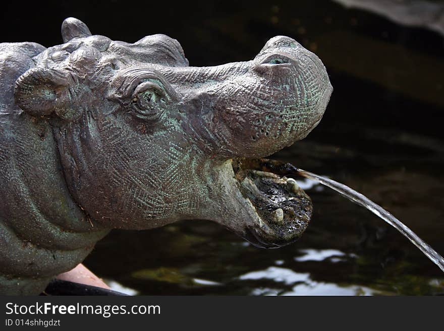 A hippo statue spits water out of its mouth into a pool.