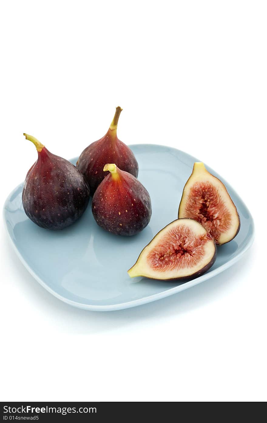 Three whole figs and one sliced one on a square blue plate