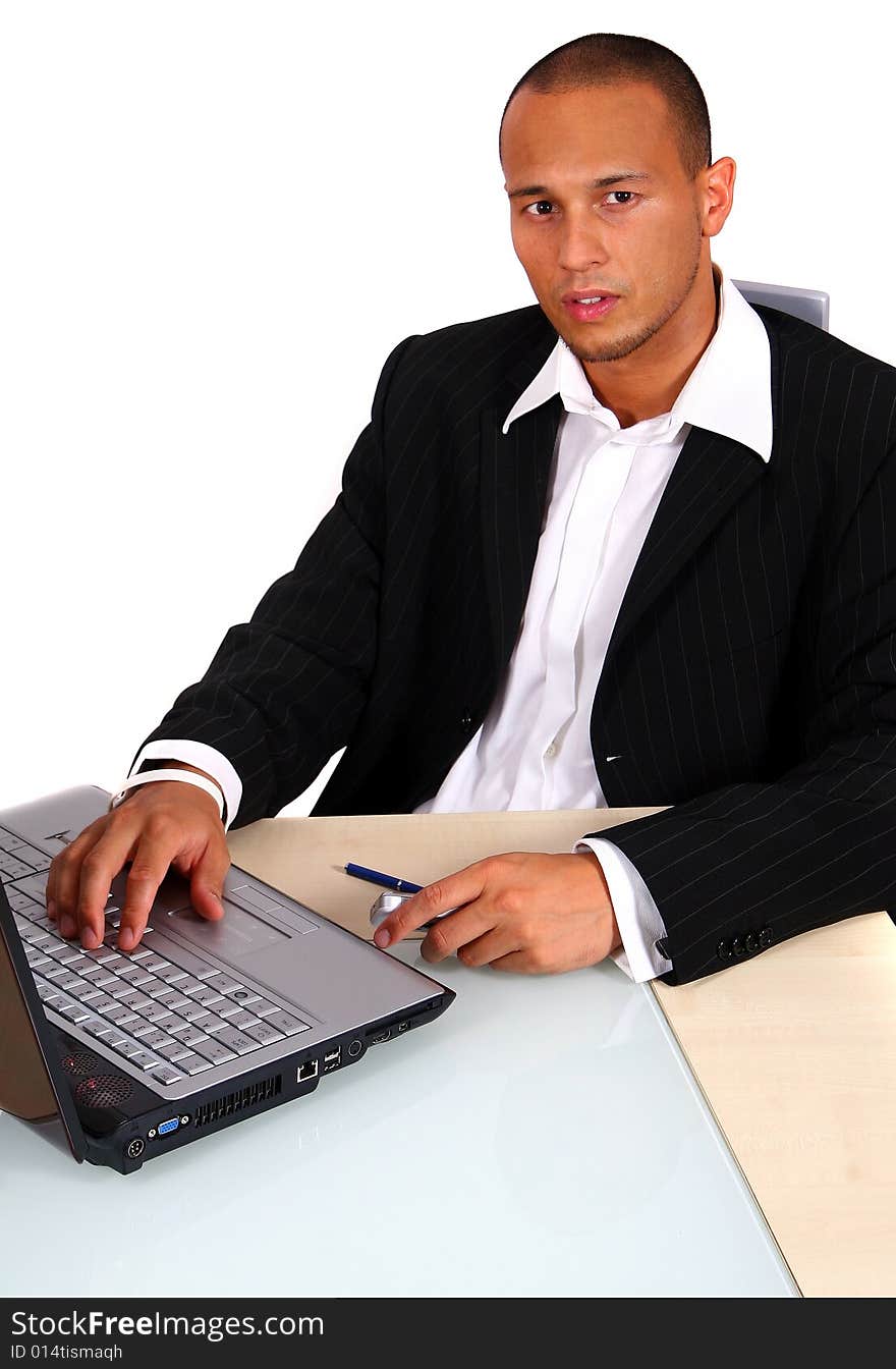 A young businessman sitting by desk at office working on the laptop with cellphone in his hand. Isolated over white. A young businessman sitting by desk at office working on the laptop with cellphone in his hand. Isolated over white.