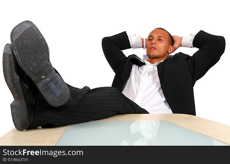 A young satisfied businessman sitting by desk at office feet on table thinking. Isolated over white. A young satisfied businessman sitting by desk at office feet on table thinking. Isolated over white.