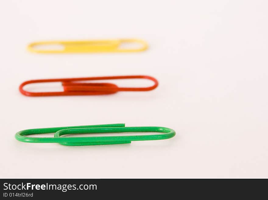 Green,red and yellow paper clips on white background shallow focal plane with front green one in focus. Green,red and yellow paper clips on white background shallow focal plane with front green one in focus