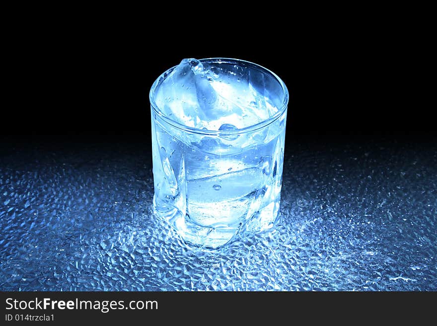 Glass of cold splashing water standing on dark background