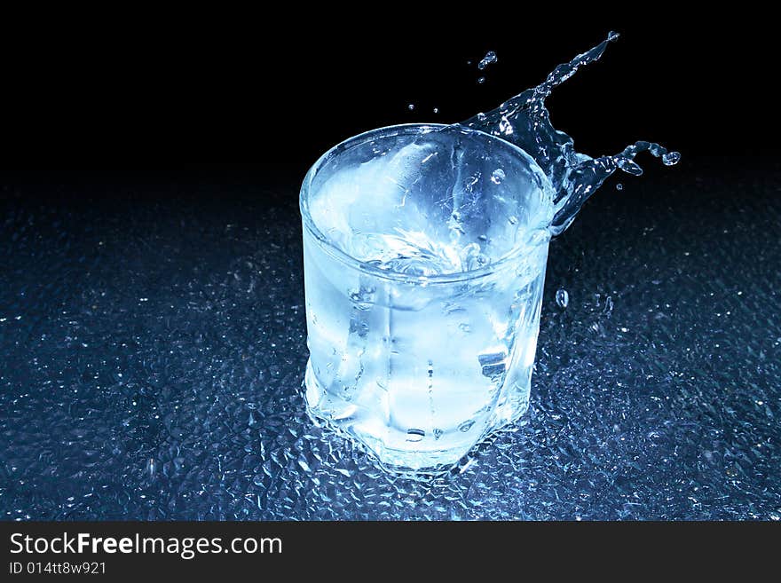 Glass of cold splashing water standing on dark background