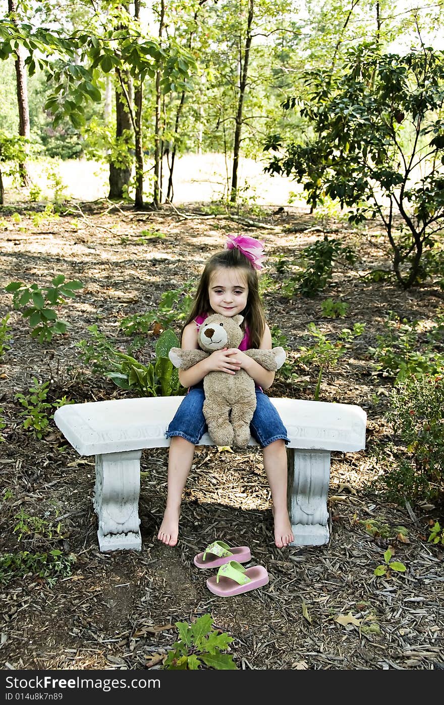 Cute little brunette girl holding her best friend a teddy bear sitting with bare feet in an outdoor setting. Cute little brunette girl holding her best friend a teddy bear sitting with bare feet in an outdoor setting.