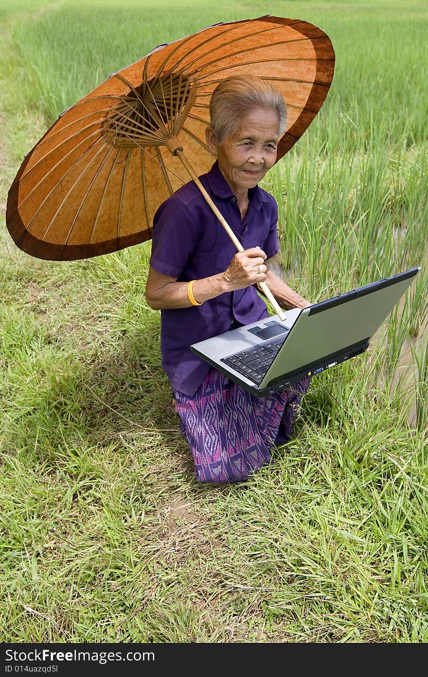 Old Asian with laptop when work in the paddy-field