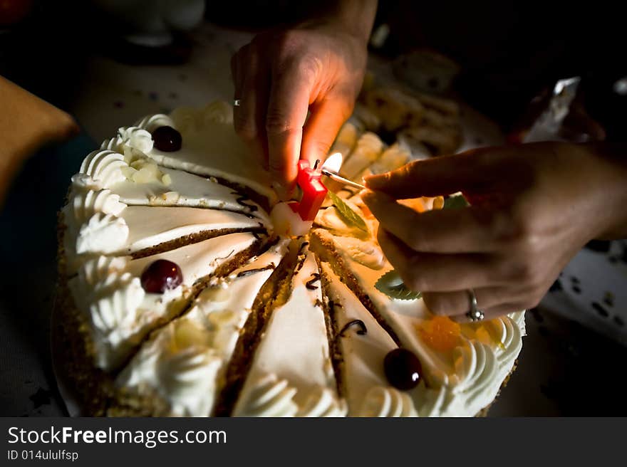 Closeup of birthday cake with hands lighting candle