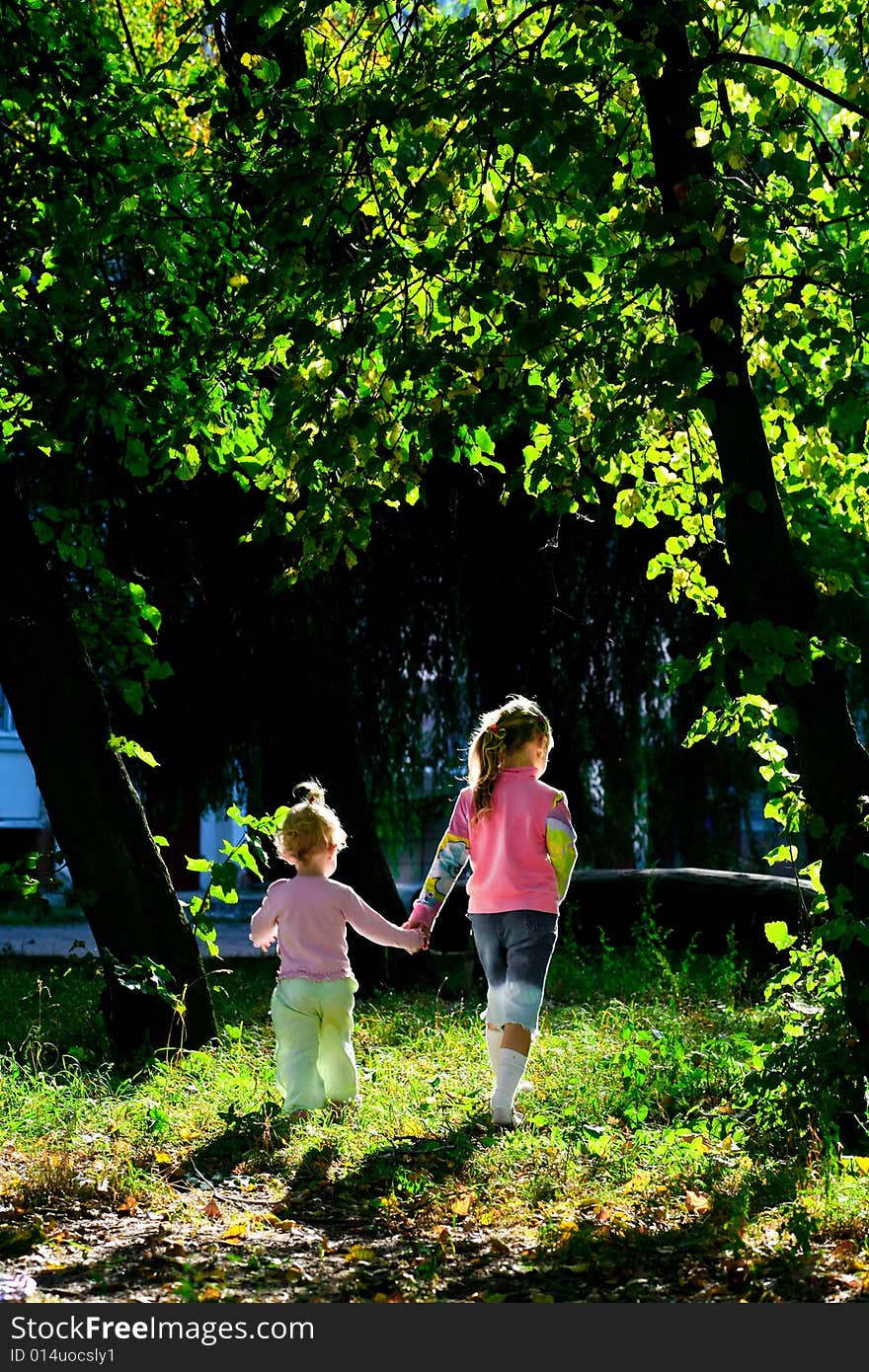 An image of two girls walking among green trees