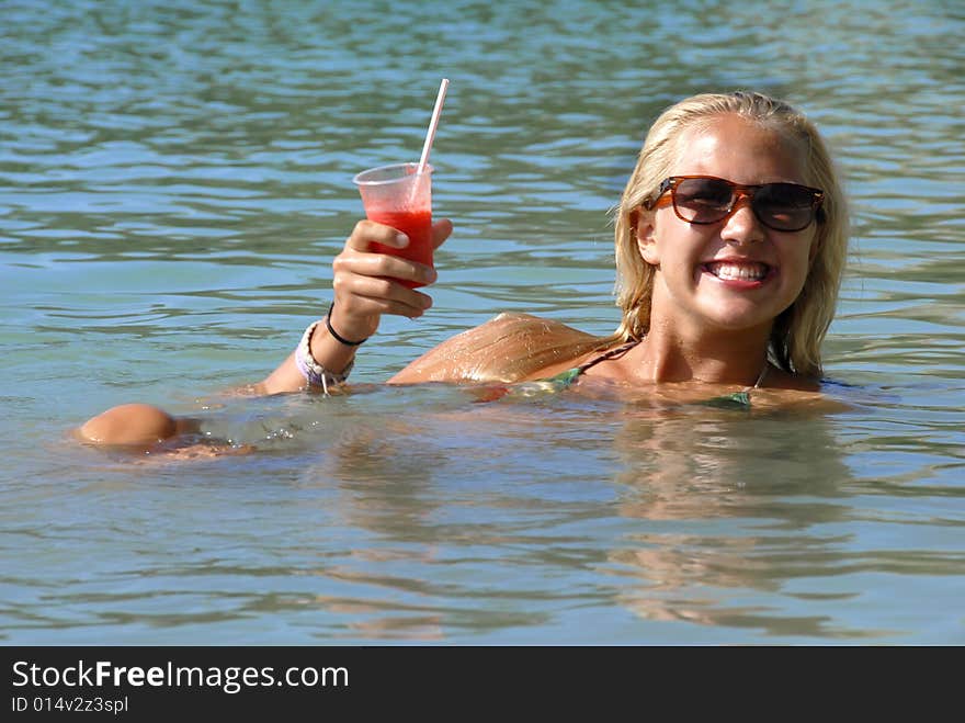 A blond girl is drinking strawberry cocktail in the water