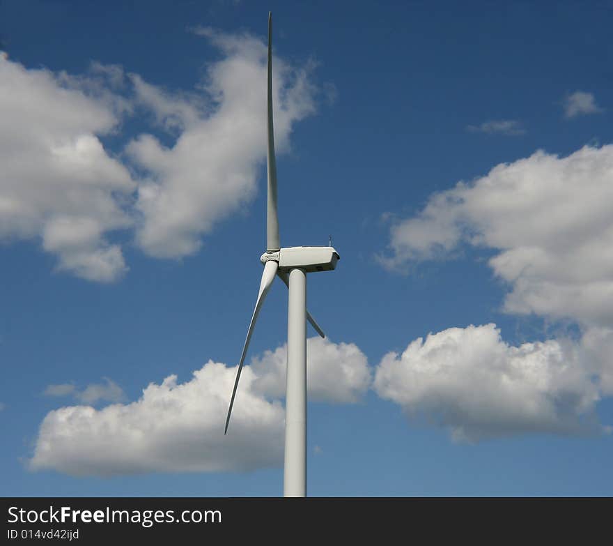 A photo  of a Wind Turbine with a blue sky and clouds in the background.