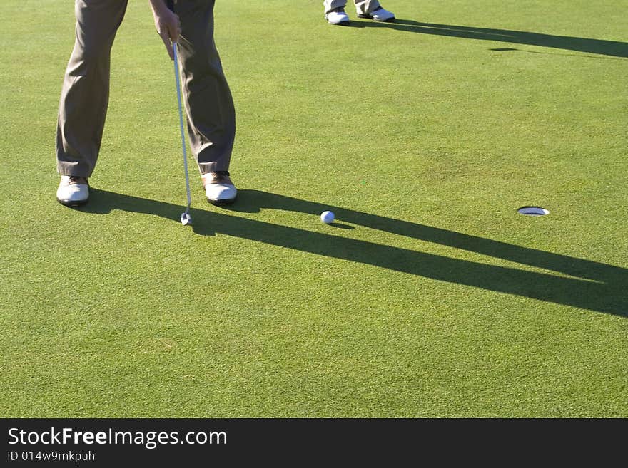 A man is standing on the green of a golf course.  He is putting the ball into the hole.  Horizontally framed shot. A man is standing on the green of a golf course.  He is putting the ball into the hole.  Horizontally framed shot.