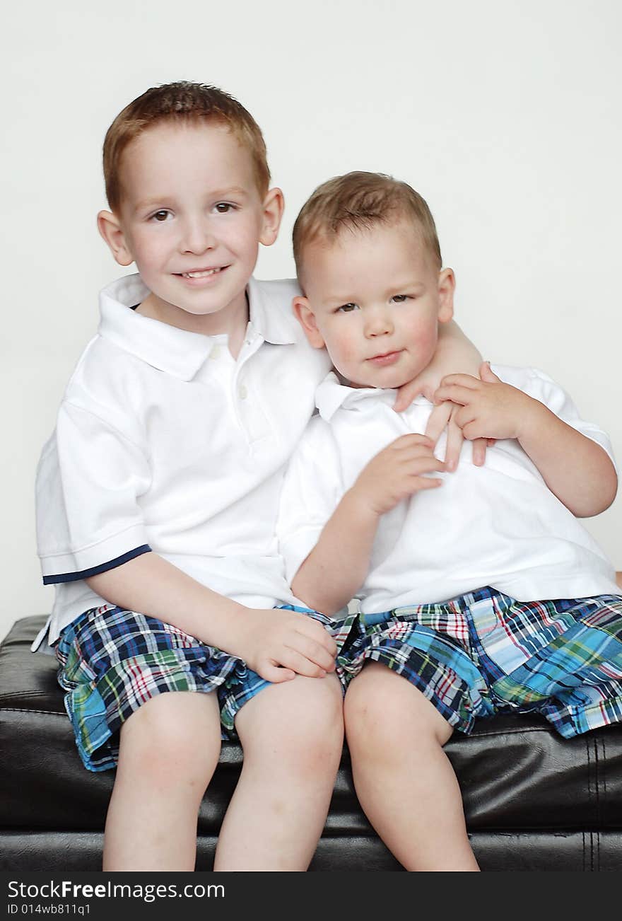 Two young brothers are posing together for a picture in a studio. They are wearing matching outfits and smiling at the camera. Vertically framed shot. Two young brothers are posing together for a picture in a studio. They are wearing matching outfits and smiling at the camera. Vertically framed shot.