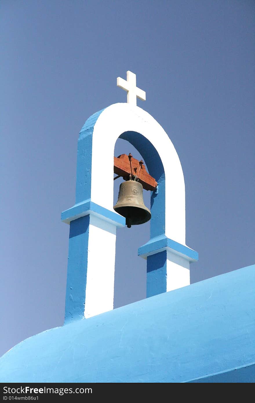 Greek church roof with cross and bell against the blue sky