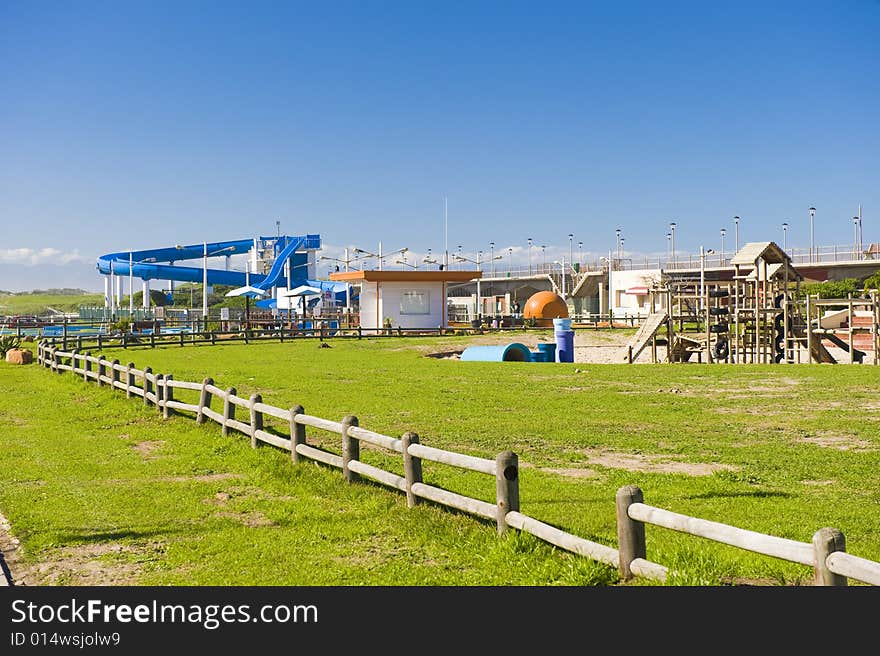 A park next to the beach with a play area for kids containing a wooden jungle-jim and a water slide. A park next to the beach with a play area for kids containing a wooden jungle-jim and a water slide.