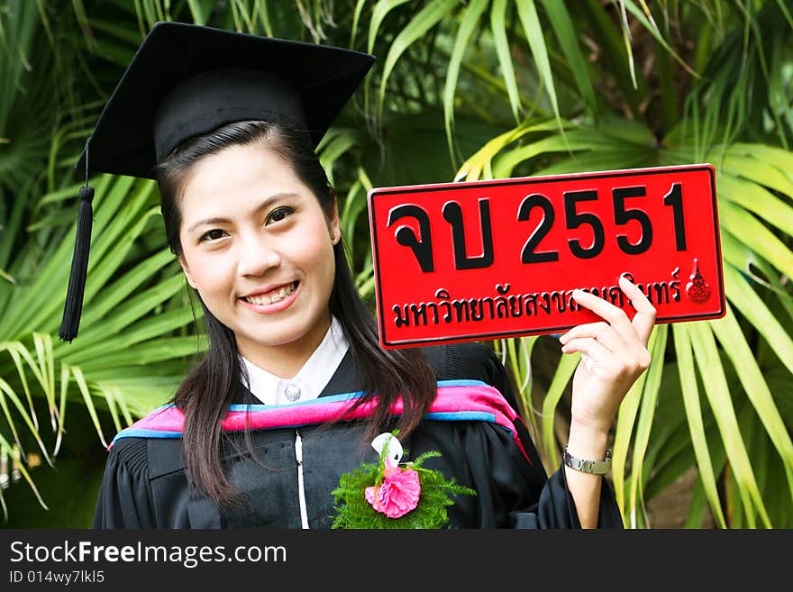 Beautiful young Asian graduate in robes on graduation day. Number plate says Happy Graduation in Thai and number refers to the year.