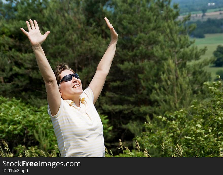 Woman with arms outstretched standing on the hill. Green forest on background. Summer. Woman with arms outstretched standing on the hill. Green forest on background. Summer.