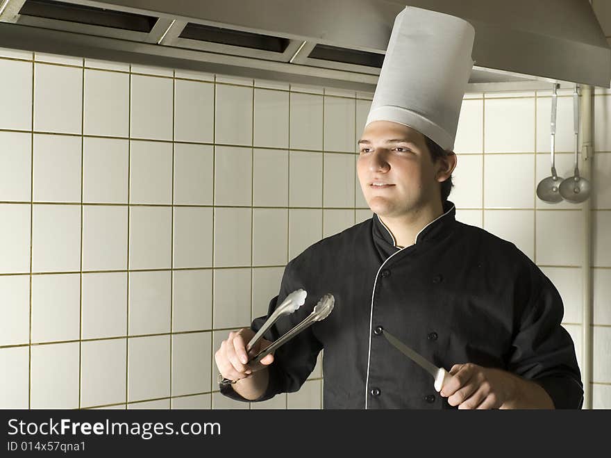 Chef holding a knife and some tongs. Vertically framed photo. Chef holding a knife and some tongs. Vertically framed photo.