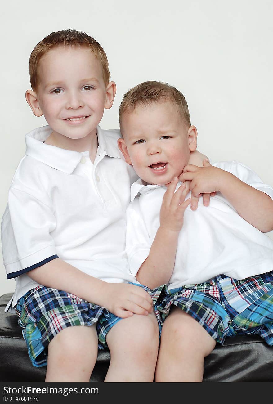 Two young brothers are posing together for a picture in a studio. They are wearing matching outfits and smiling at the camera.  Vertically framed shot. Two young brothers are posing together for a picture in a studio. They are wearing matching outfits and smiling at the camera.  Vertically framed shot.