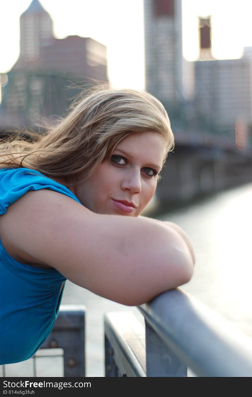 Young woman leaning against a bridge with buildings in the background smiling a sly smile. Vertically framed photo. Young woman leaning against a bridge with buildings in the background smiling a sly smile. Vertically framed photo.