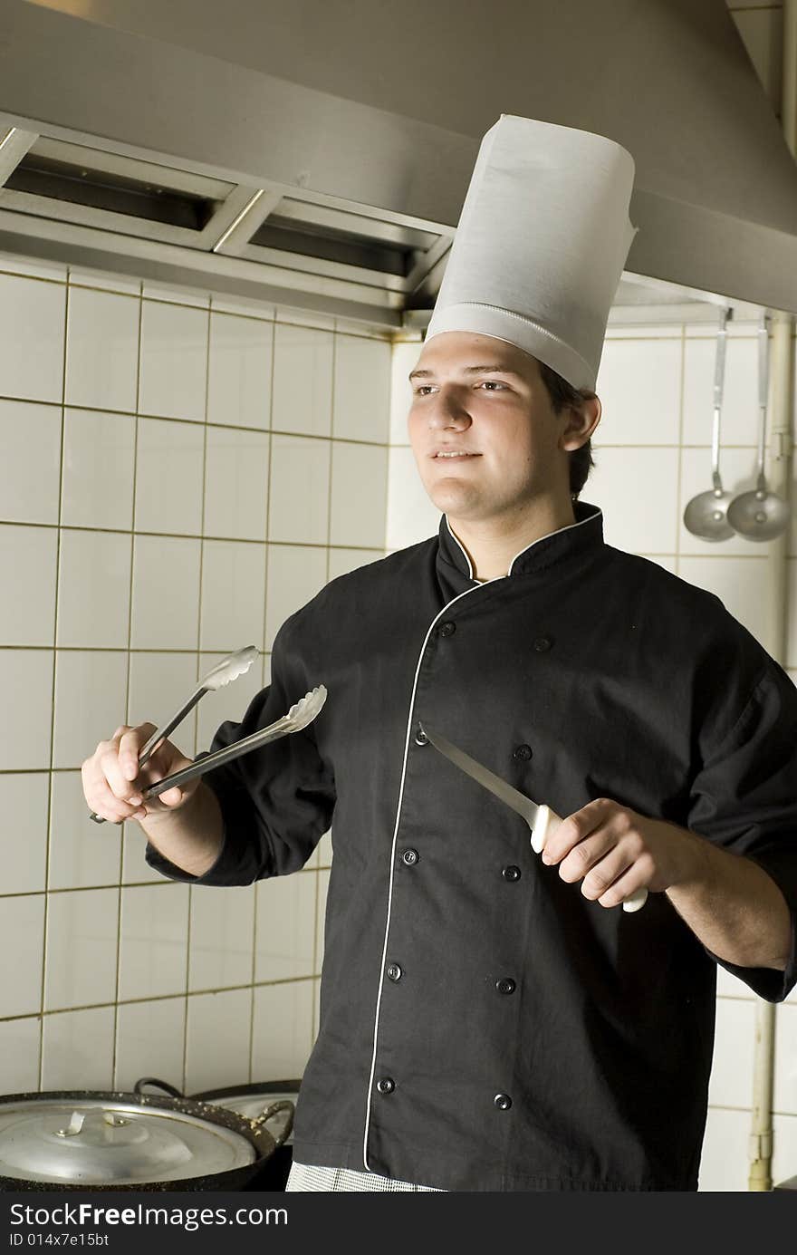 Smiling chef holding a knife and some tongs. Vertically framed photo. Smiling chef holding a knife and some tongs. Vertically framed photo.