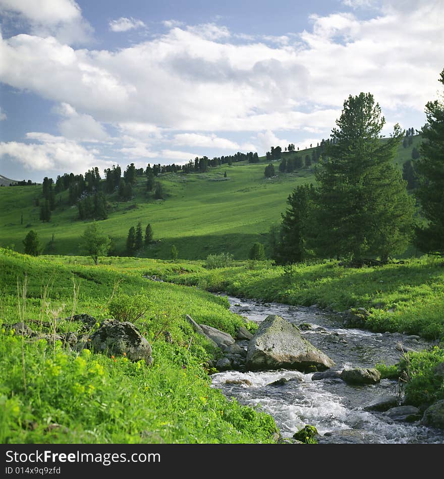 River flow in high mountains, green grass, water and clouds