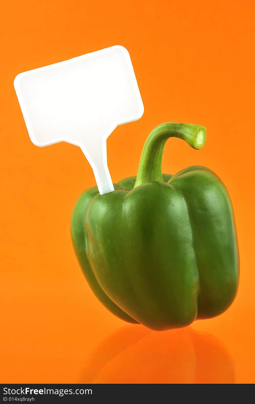 Green paprika against orange background with price tag