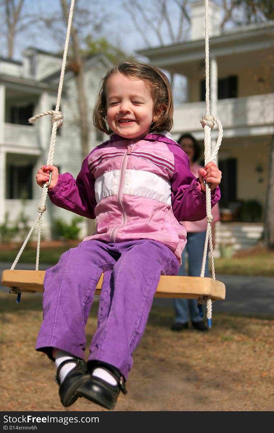 Cute little girl swinging on rope swing, mom out of focus in background