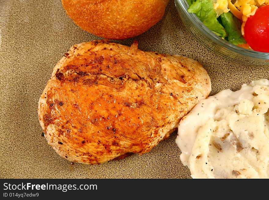 Grilled chicken, mashed potatoes, rolls and salad in plate.