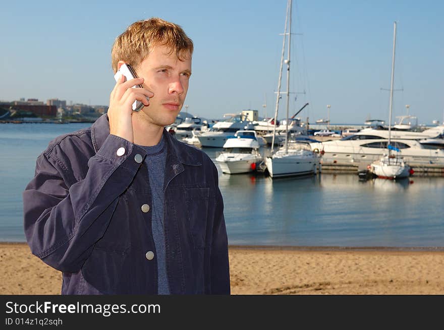 Young stylish man talk on mobile phone with yacht background.