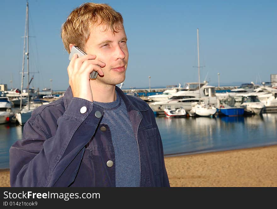 Young stylish man talk on mobile phone with yacht background.