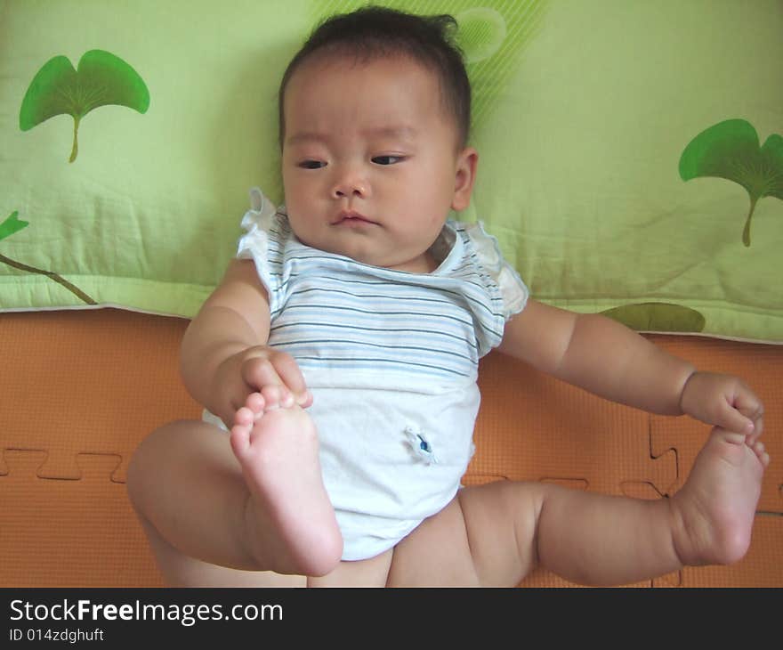 Lovely baby is lying down on a pillow playing her feet