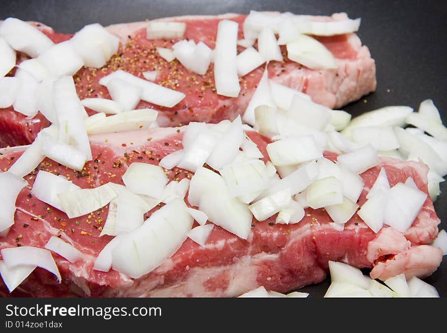 Fresh strip steaks smothered in onions in a pan. Fresh strip steaks smothered in onions in a pan