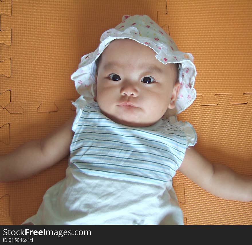 Pretty big eyes baby with a cute expression on a yellow mat. Pretty big eyes baby with a cute expression on a yellow mat