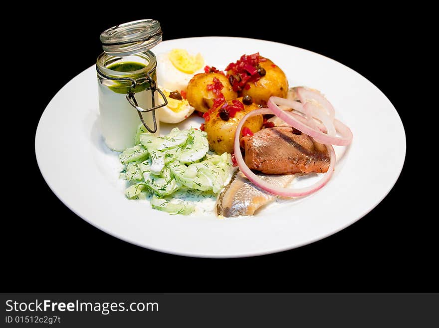 Herring with boiled potatos and cucumber salad on a white plate isolated on black