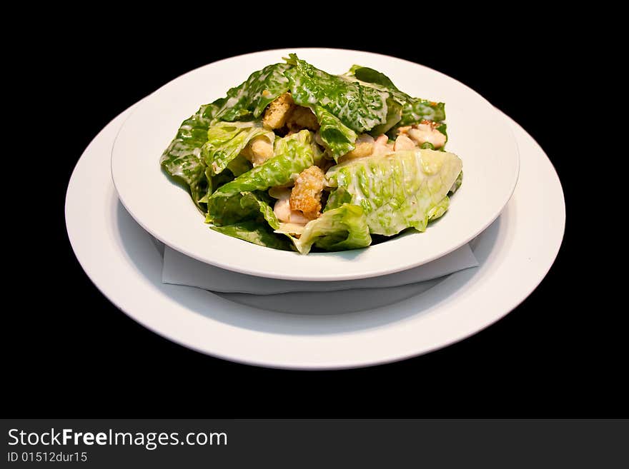 Caesar salad with shrimps on a white plate isolated on black