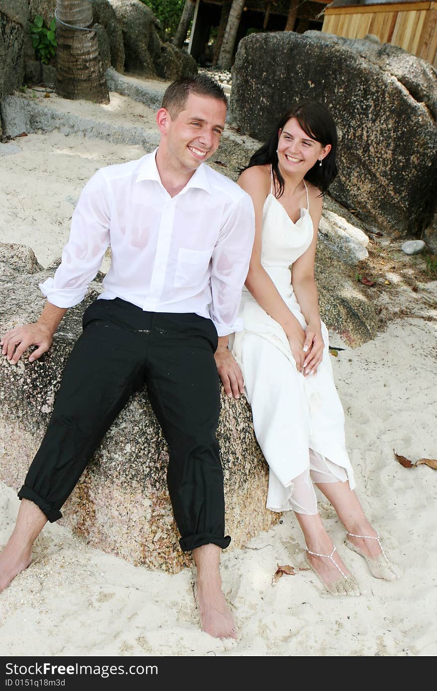 Bride and groom sitting on a rock at the beach.