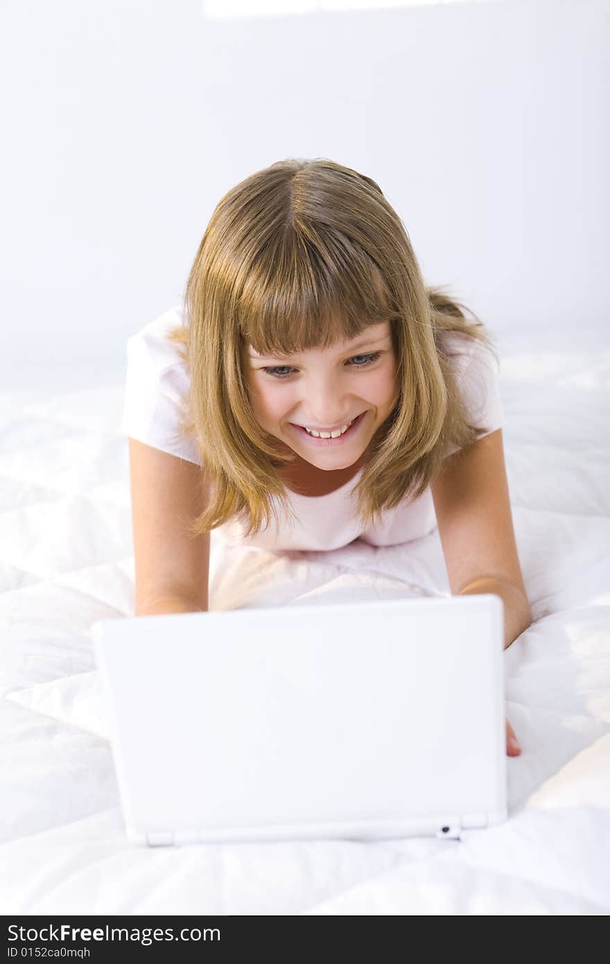 Young smiling girl lying on a bed and does something on laptop. Young smiling girl lying on a bed and does something on laptop.