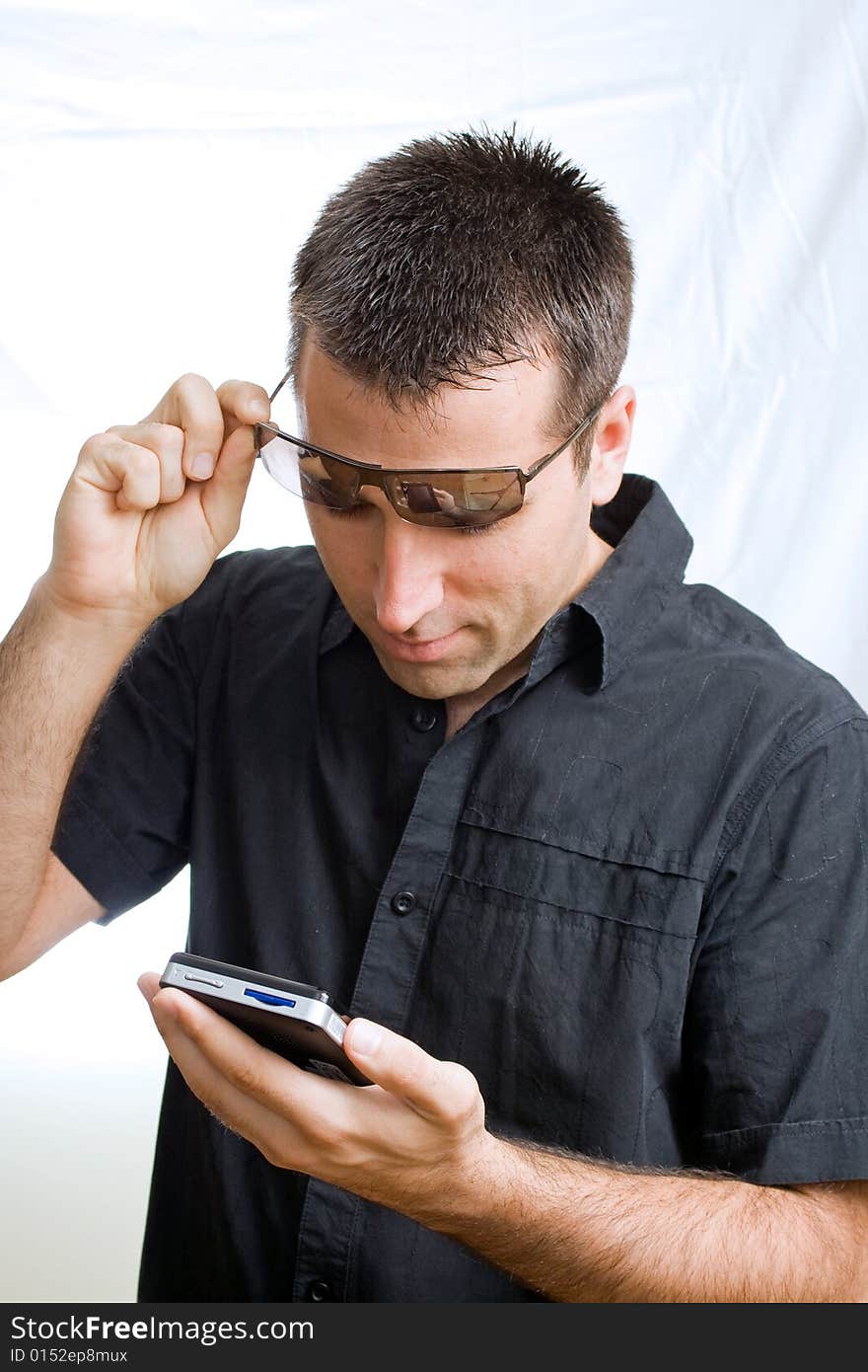 A young man, wearing sunglasses, looking at his cellphone(mobile), smiling. A young man, wearing sunglasses, looking at his cellphone(mobile), smiling