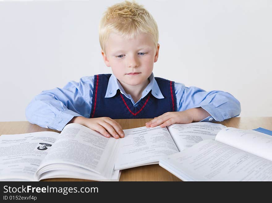 Young boy sitting at desk and reading books. Front view. Young boy sitting at desk and reading books. Front view.