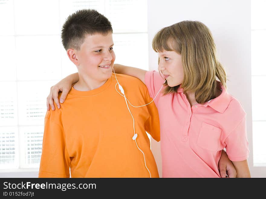 Boy and girl standing in front of window and listening to music by earphones. They smiling and looking each other. Boy and girl standing in front of window and listening to music by earphones. They smiling and looking each other.