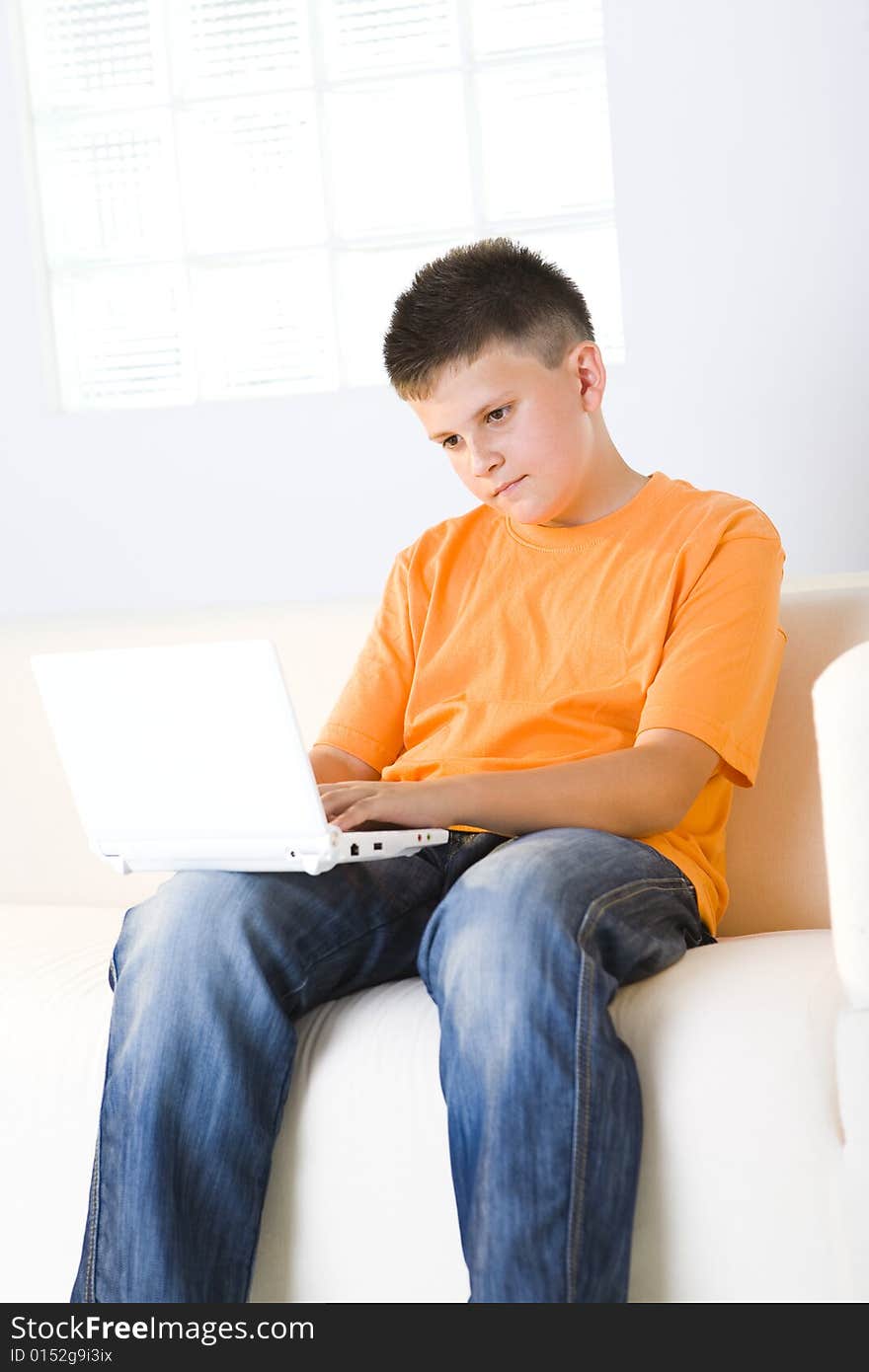 Young boy with laptop sitting on couch. He looks unhappy.