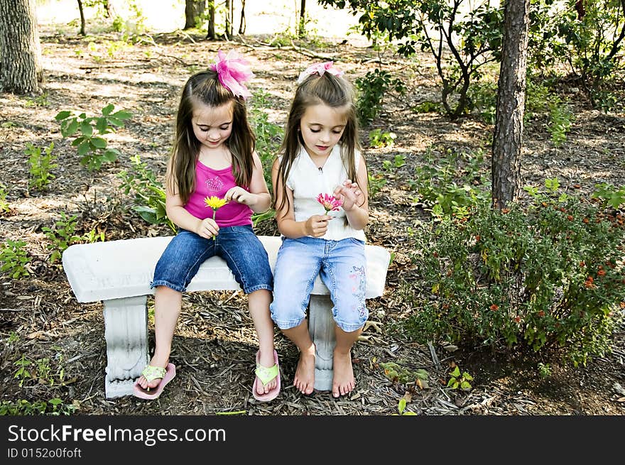 Two little girls pulling pedals from their flowers saying he loves me, he loves me not.