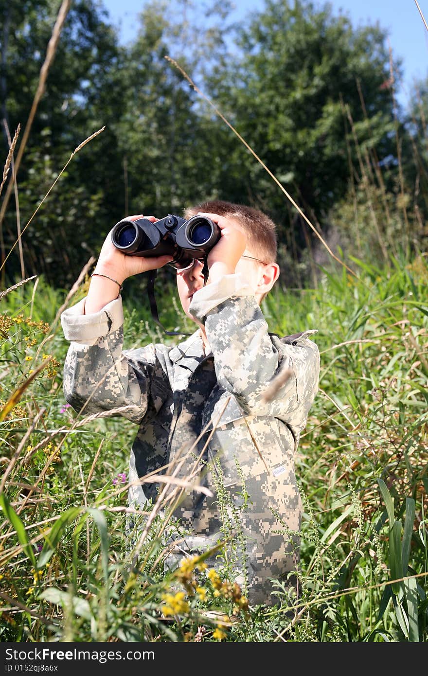 Young boy in field, in camofllage, looking up through binoculars. Young boy in field, in camofllage, looking up through binoculars