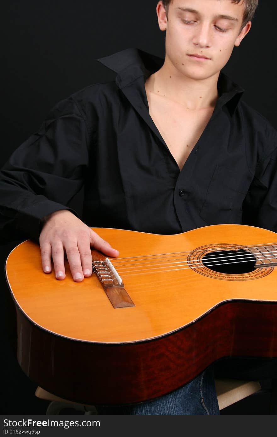 Teenage male in casual attire holding a guitar. FOCUS ON GUITAR by HAND. Teenage male in casual attire holding a guitar. FOCUS ON GUITAR by HAND