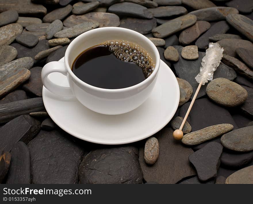 Cup of coffee against black stones and reed sugar