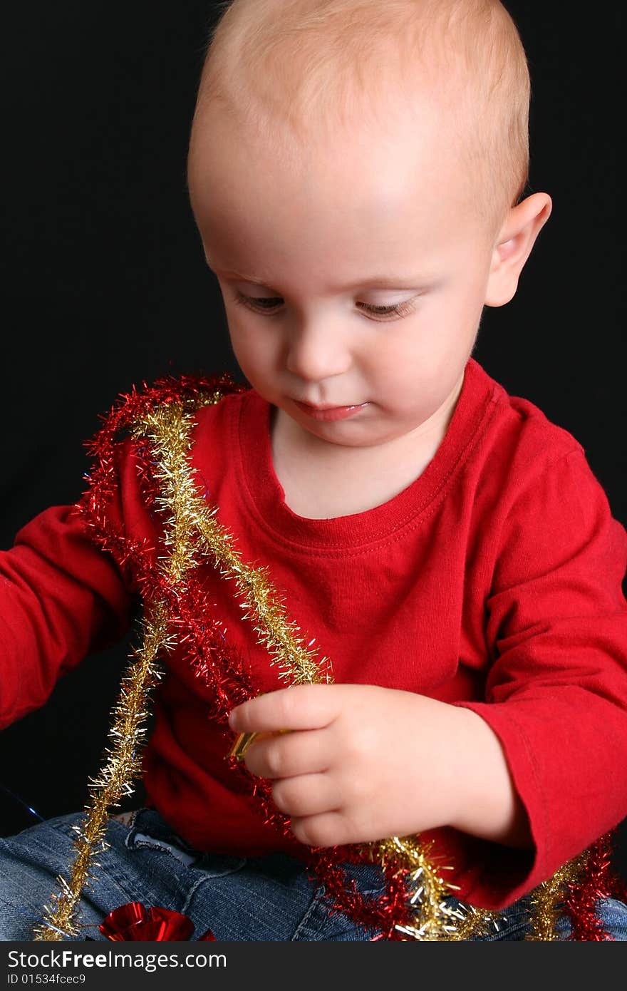 Toddler against a black background playing with Christmas decorations