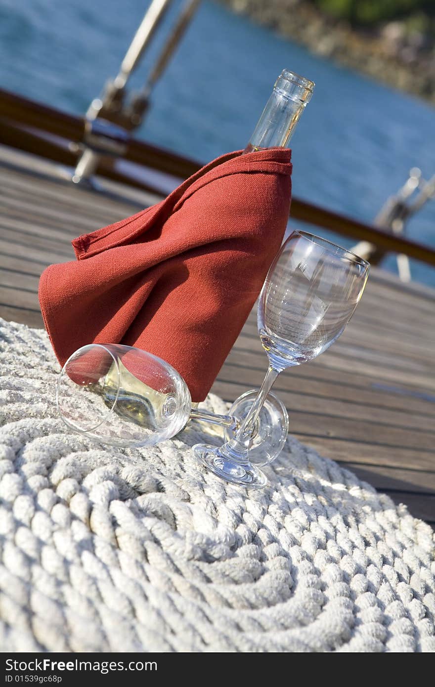 A bottle of wine and glasses on the wooden deck of a yacht. A bottle of wine and glasses on the wooden deck of a yacht