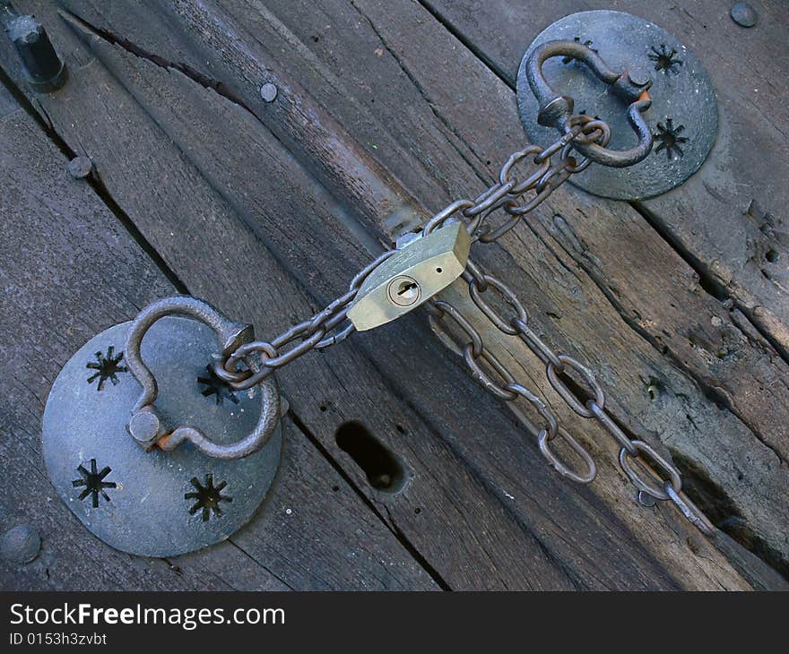 Old pig-iron chain with new lock on the old wood door. Old pig-iron chain with new lock on the old wood door