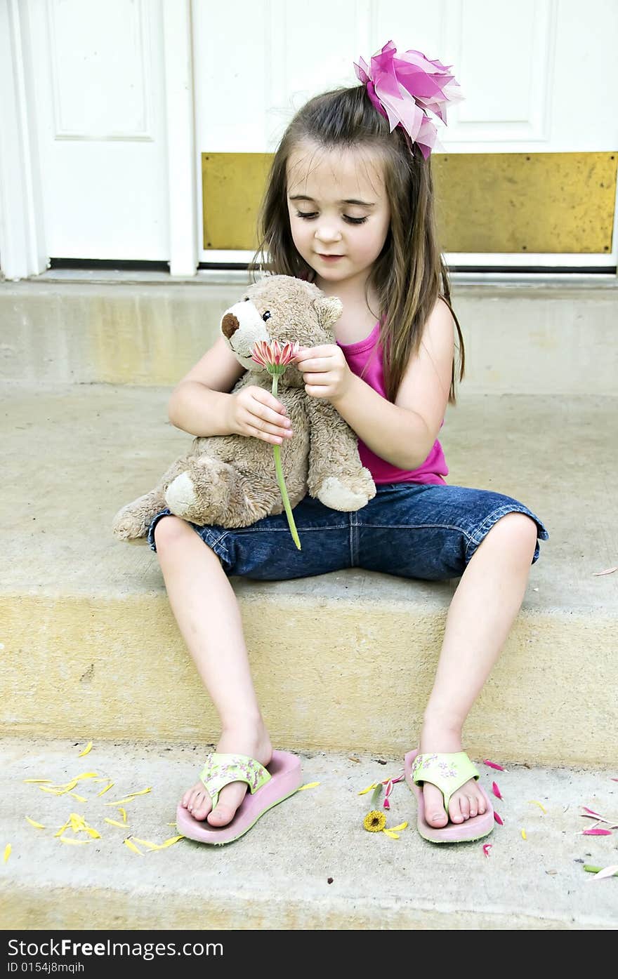 Little girl plucking pedals from a flower holding her bear trying to decide if he does or doesn't love her. Little girl plucking pedals from a flower holding her bear trying to decide if he does or doesn't love her.