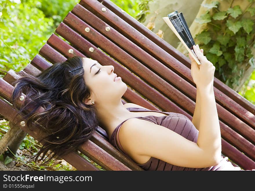 Reading woman laying in a park bench. Reading woman laying in a park bench.