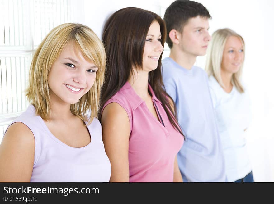 Group of friends standing at the wall. First girl looking at camera. Focused on first girl. Group of friends standing at the wall. First girl looking at camera. Focused on first girl.